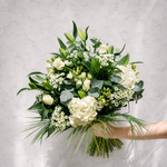 A bouquet of white flowers and green foliage held by a person's arm against a light gray marble-textured background.