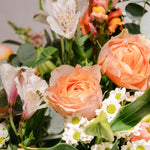 A close-up of a floral arrangement featuring peach roses, white alstroemeria, and green eucalyptus leaves against a soft neutral background.