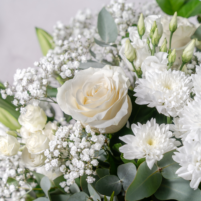 Close up of Tranquility white bouquet showing white roses, lilies and gypsophilia in an elegant sympathy and get well arrangement