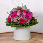 Signature Hatbox flower arrangement showing roses, germini, daisy chrysanthemums and waxflowers in pink and purple tones presented in a luxury hatbox for delivery across Ireland